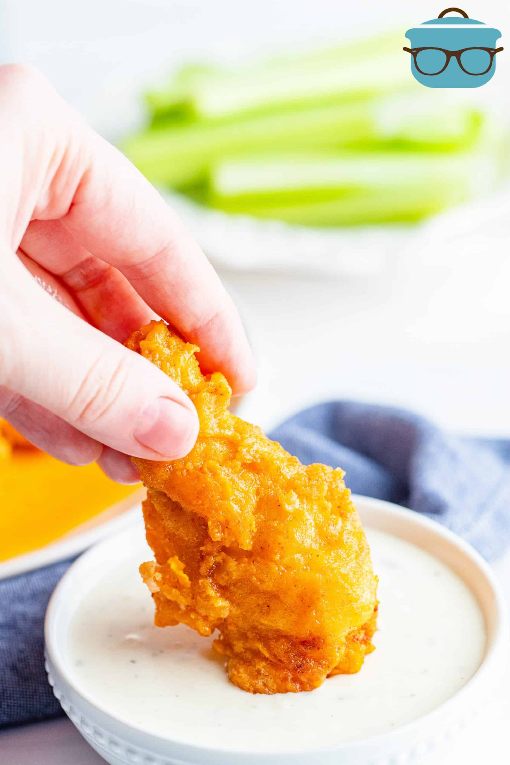 dipping one buffalo chicken wing into a bowl of ranch dressing.