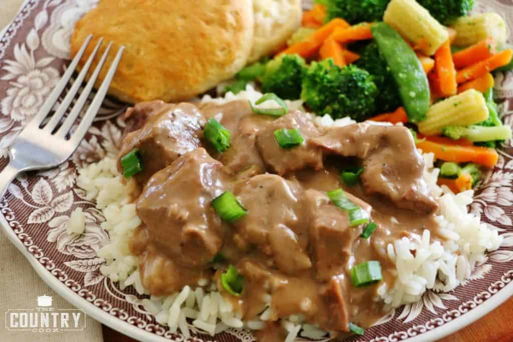 overhead photo of beef tips served over rice on a plate with vegetables and a biscuit. 