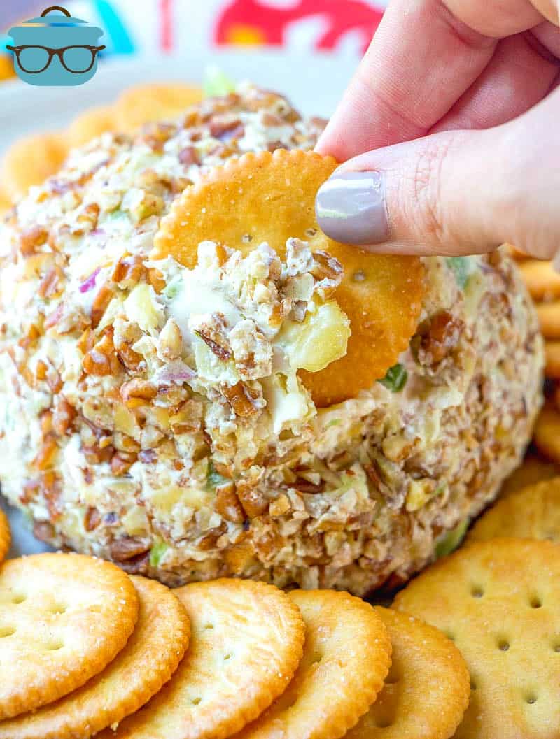 hand shown dipping a Ritz cracker into cheeseball surrounded by additional butter crackers.