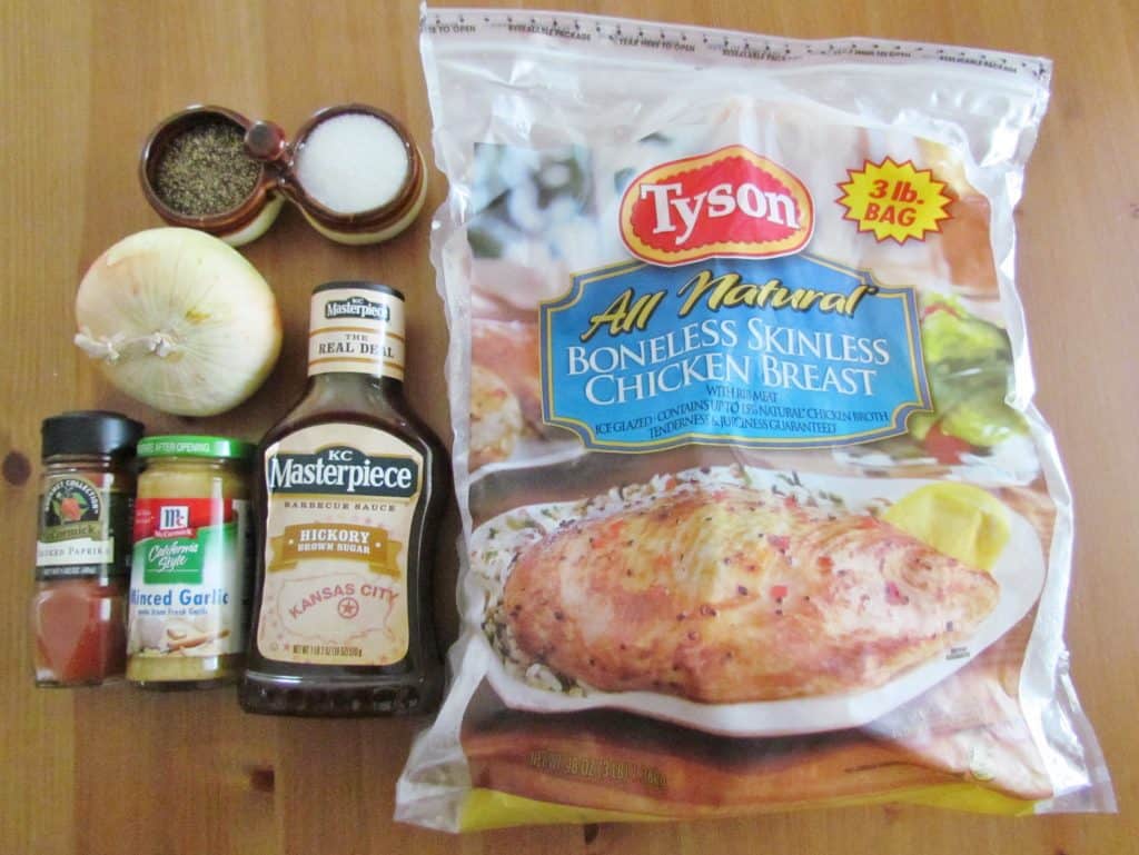 Crock Pot Shredded BBQ Chicken ingredients shown: bag of frozen chicken breasts, onion, garlic, smoked paprika, salt and pepper