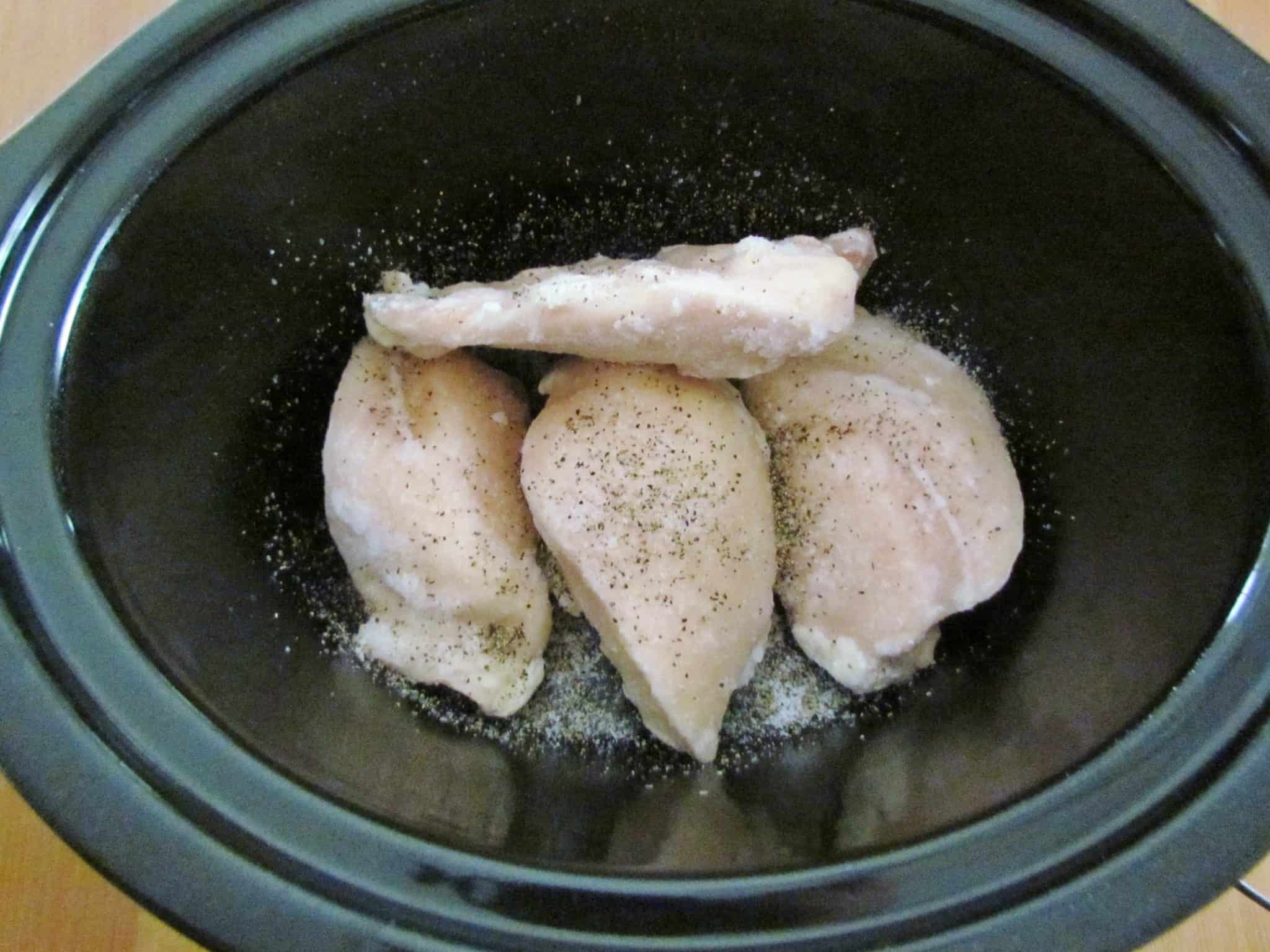 frozen chicken breasts shown in an oval crock pot.