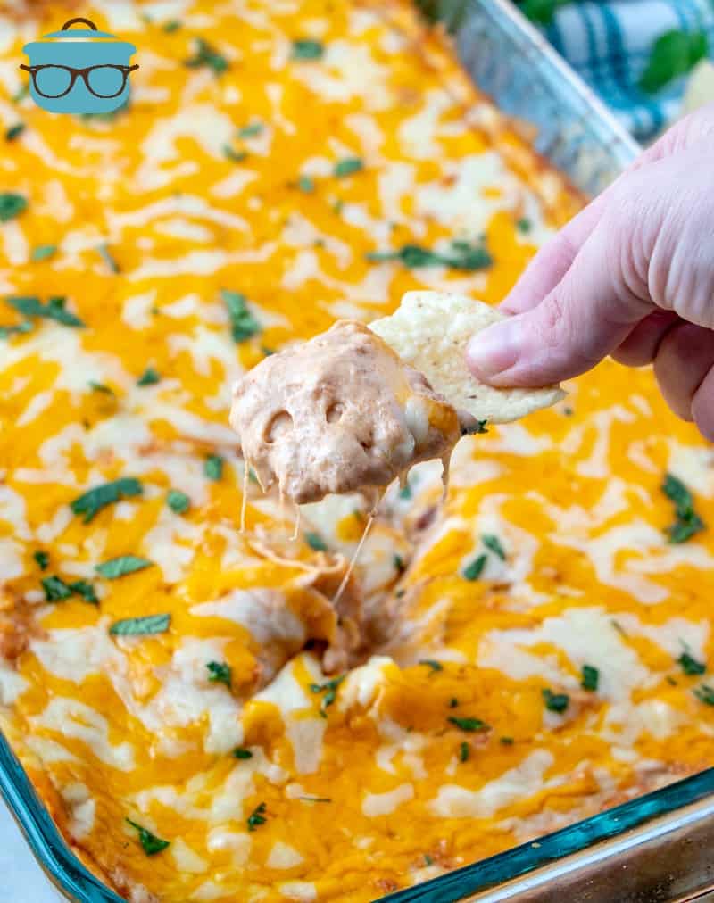 a hand scooping up bean dip with a tortilla chip. 