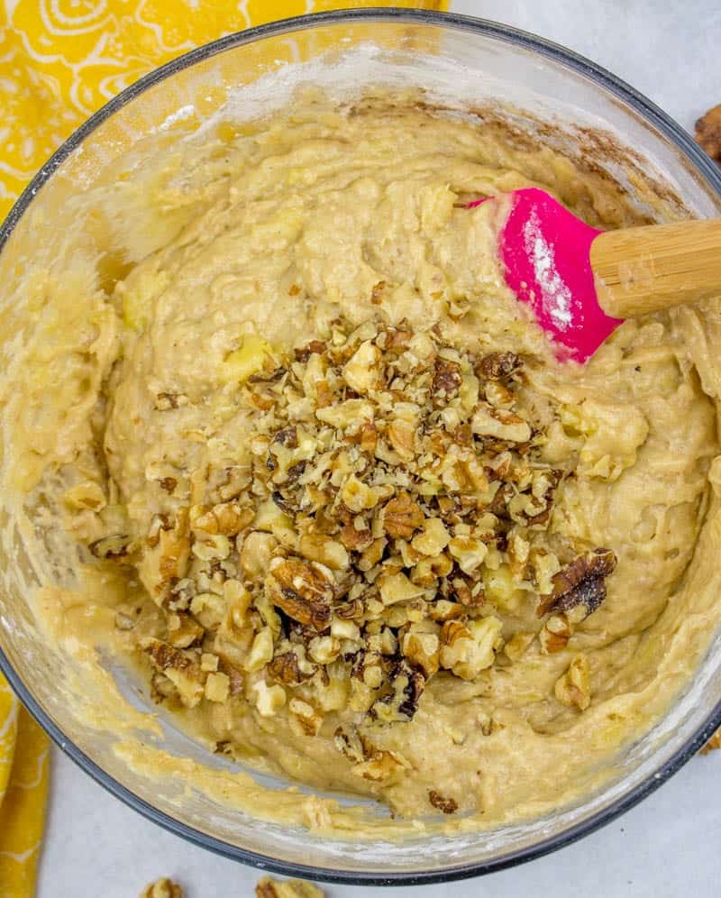 stirring in chopped walnuts to banana bread batter in a bowl with a pink spoon.