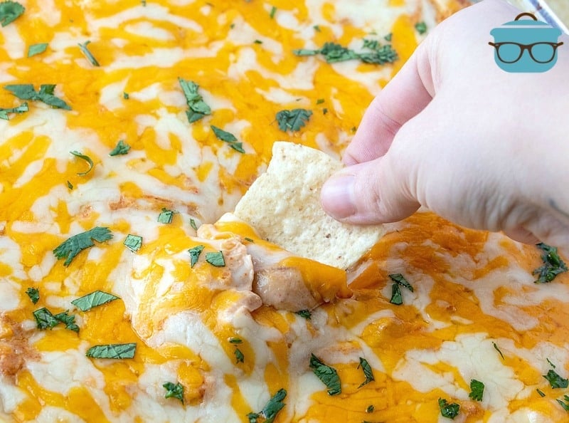 a hand scooping a tortilla chip into bean dip.