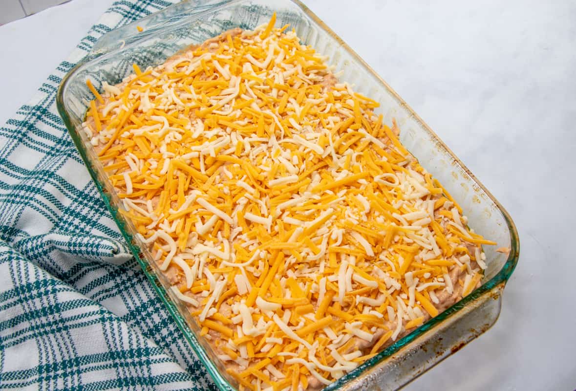 warm bean dip mixture spread into baking dish topped with shredded cheeses.