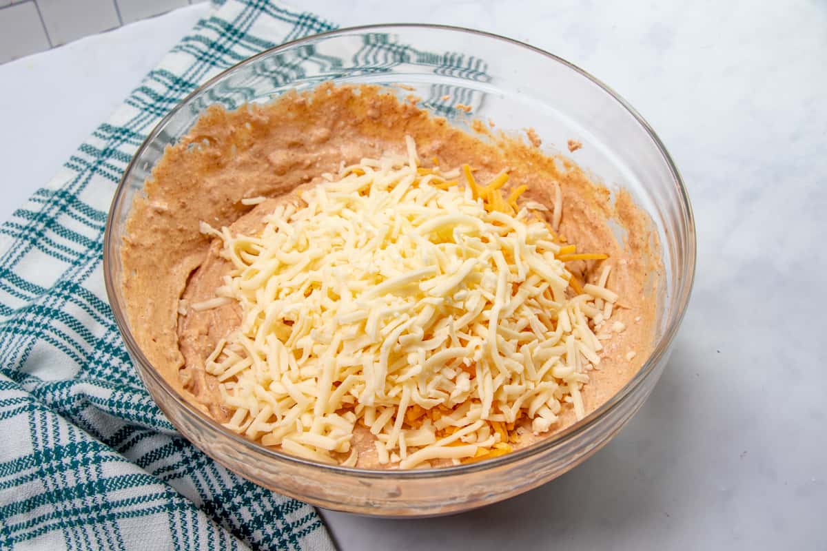 salsa, taco seasoning and cheese added to refried bean mixture in a bowl.
