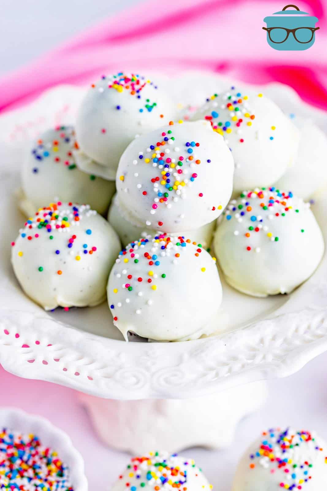 Oreo balls with sprinkles shown on a white cake stand. 