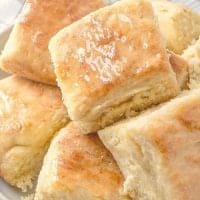 Easy Yeast Biscuit rolls piled on a plate with melted butter on top