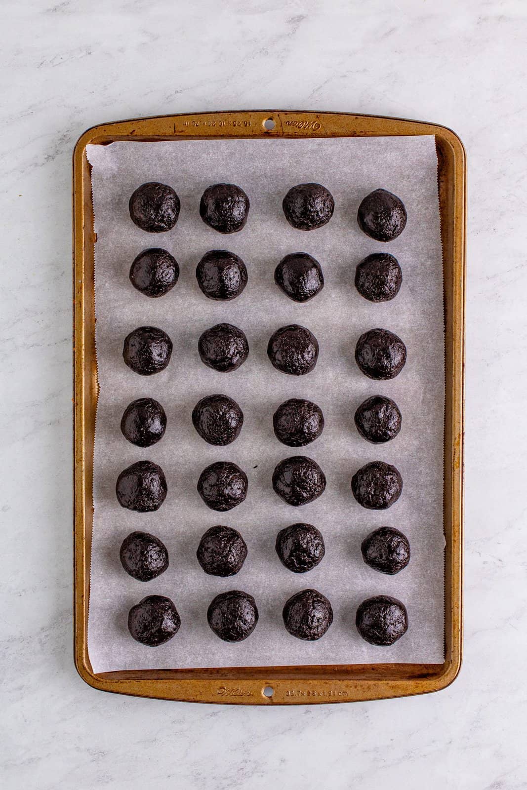 cookie balls shown on parchment paper on a cookie sheet.