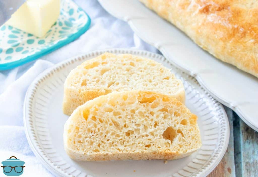 Easy Homemade French Bread, sliced on a plate with butter pictured in the background.
