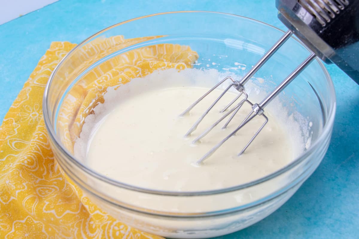 hot milk sponge cake batter in a bowl mixed with an electric mixer.