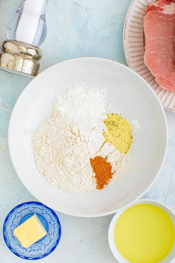 flour, cornstarch, lemon pepper seasoning and cajun seasoning shown in a shallow white bowl.