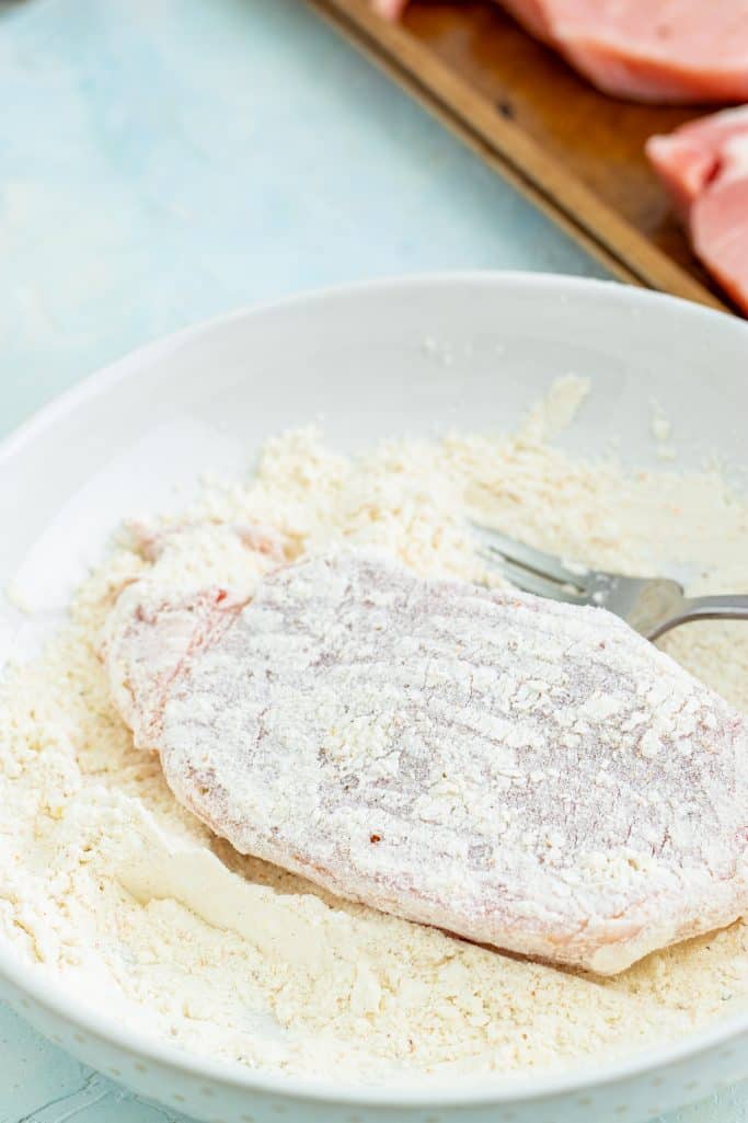shown is a raw pork chop being covered in flour.