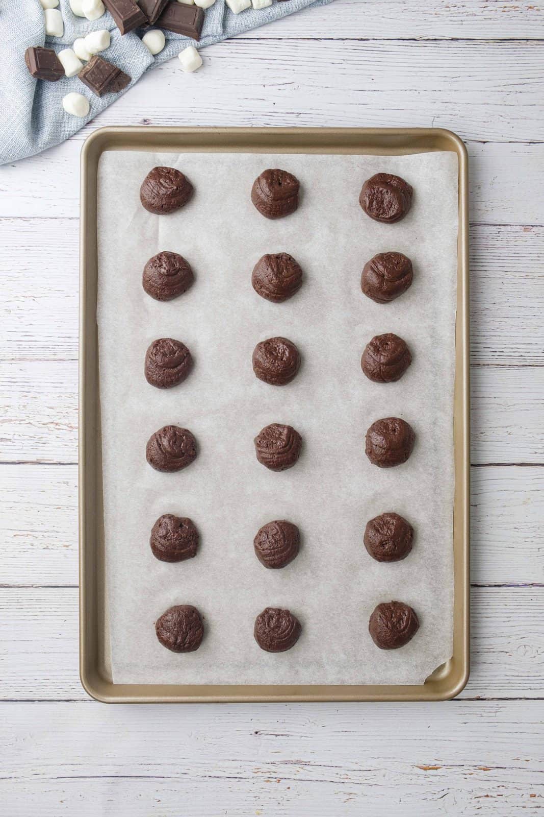 chocolate batter balls on a baking sheet that has been lined with parchment paper. 