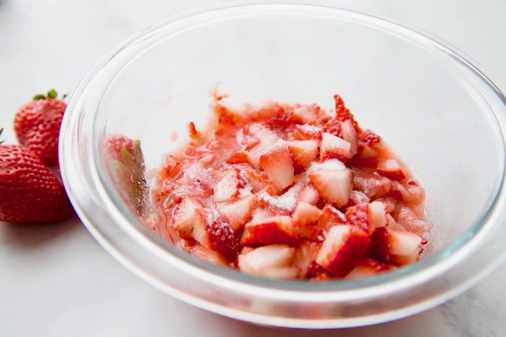 diced strawberries mixed with sugar in a glass bowl.