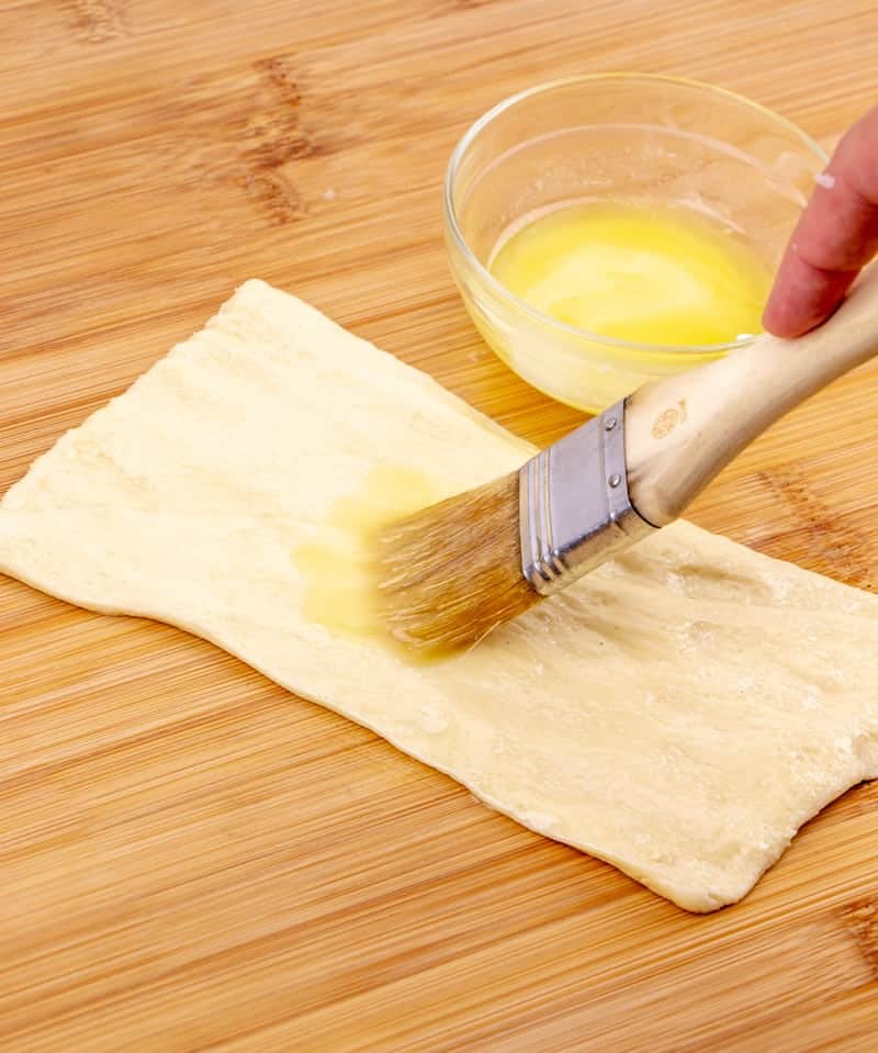 pastry brush brushing melted butter on crescent roll dough.