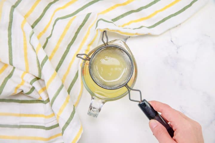 a small strainer being held over a small cup of lemon juice.