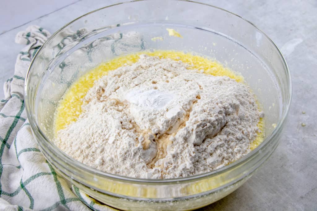 flour, baking soda and baking powder added to wet ingredients in a large glass bowl