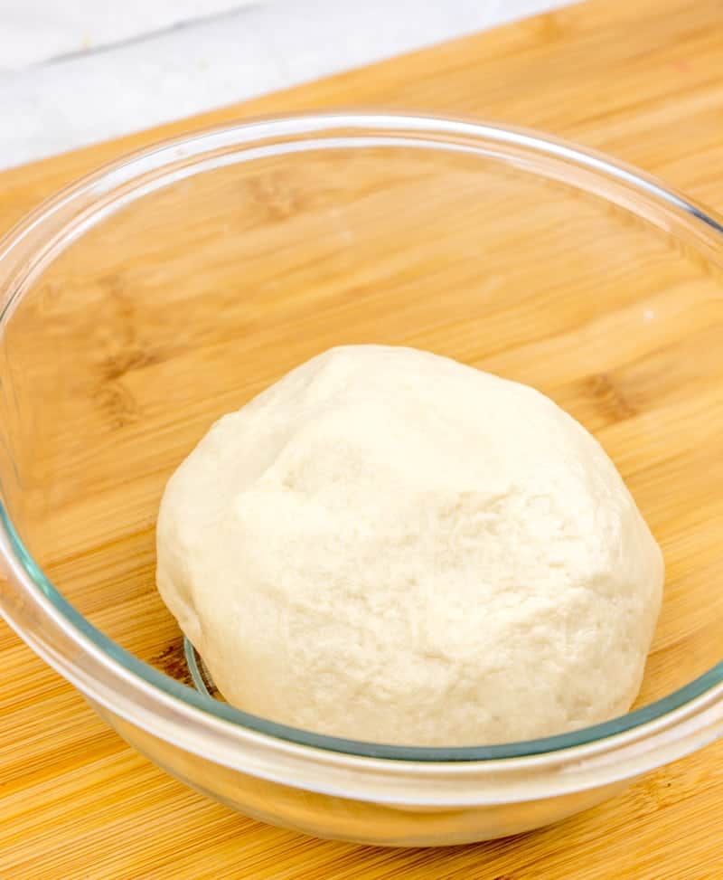 flour tortilla dough rolled into a ball in a glass bowl.