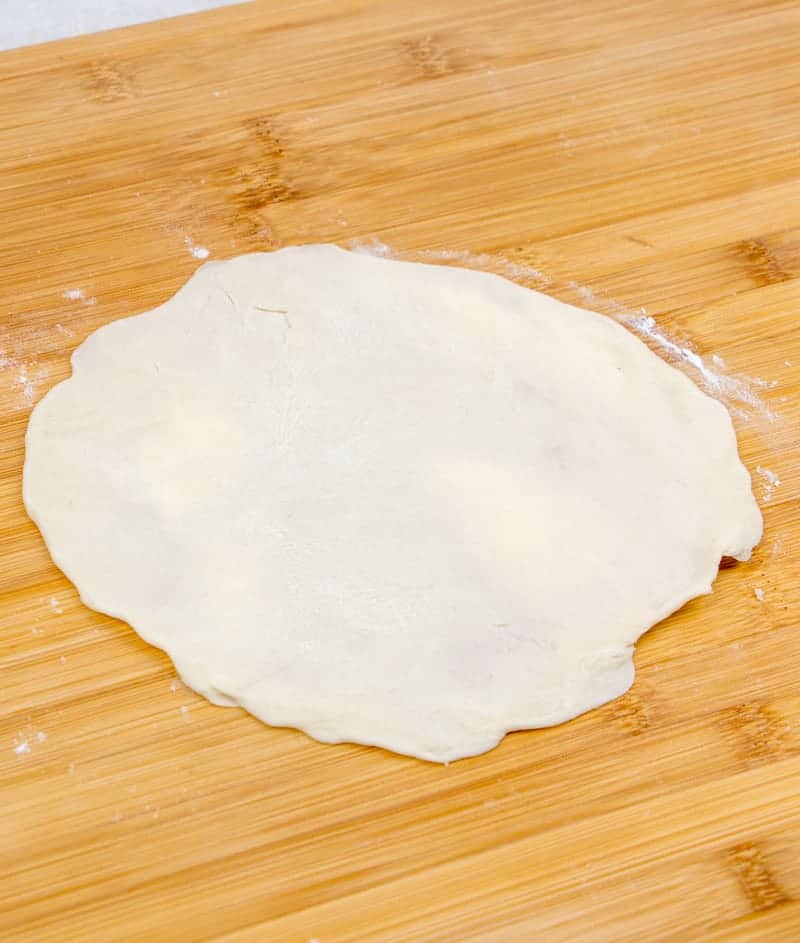 rolled out homemade flour tortilla dough on a wooden cutting board.