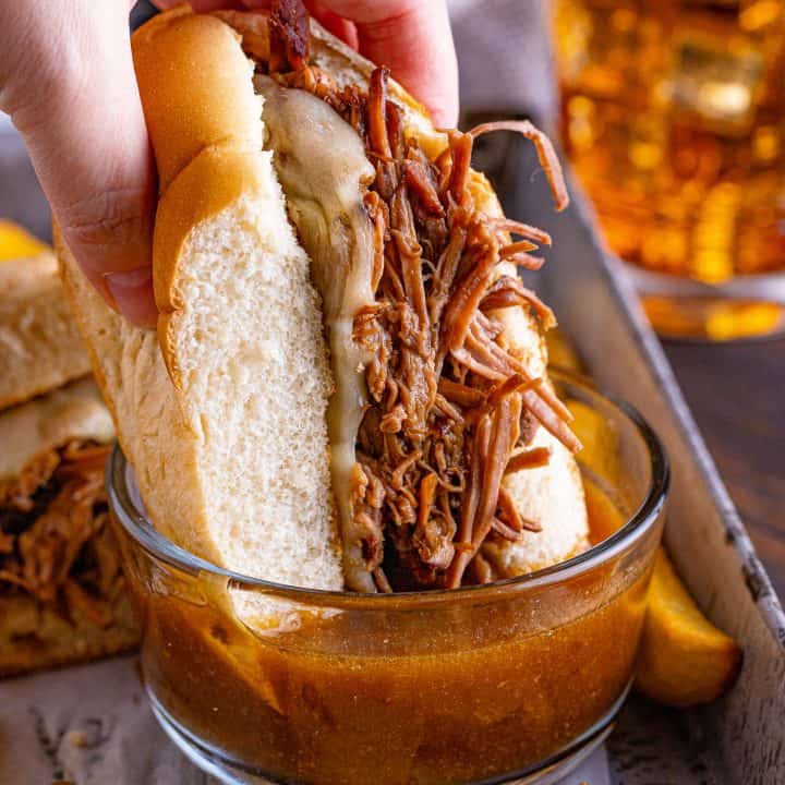 closeup photo of a hand dipping a French dip into some gravy.