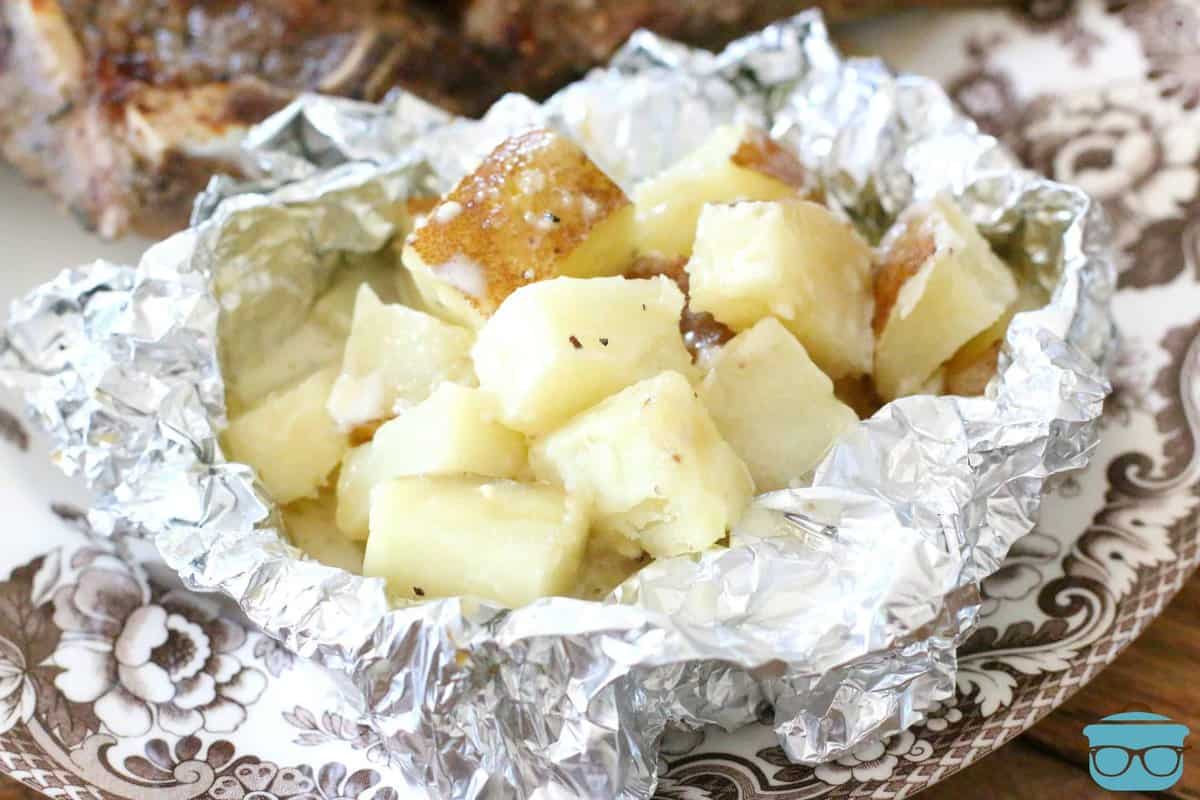 potatoes shown in aluminum foil on a plate with a steak.