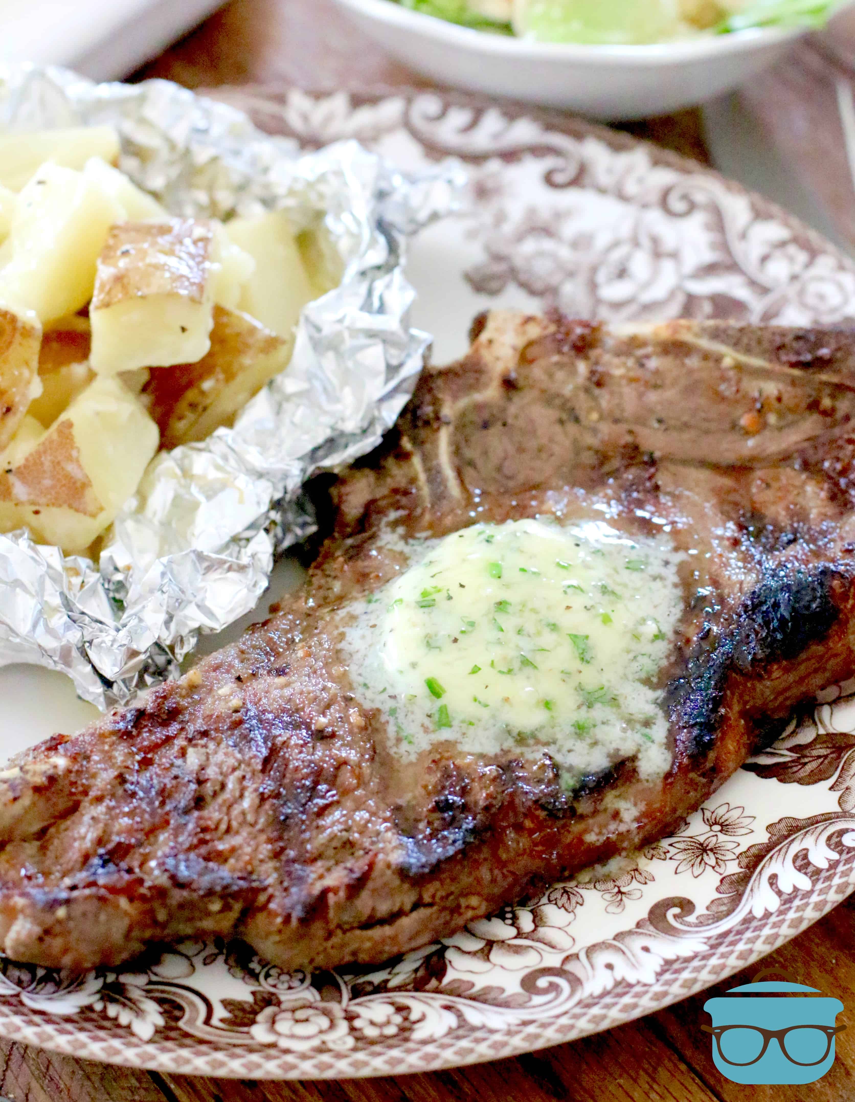 grilled steak with melted butter on top and garlic potato packages shown on the side. 