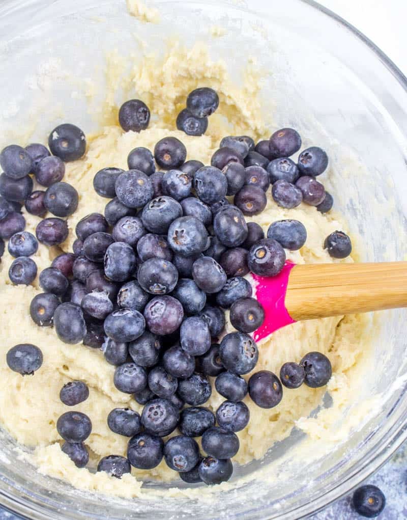 fresh blueberries added to cake batter in a glass bowl.