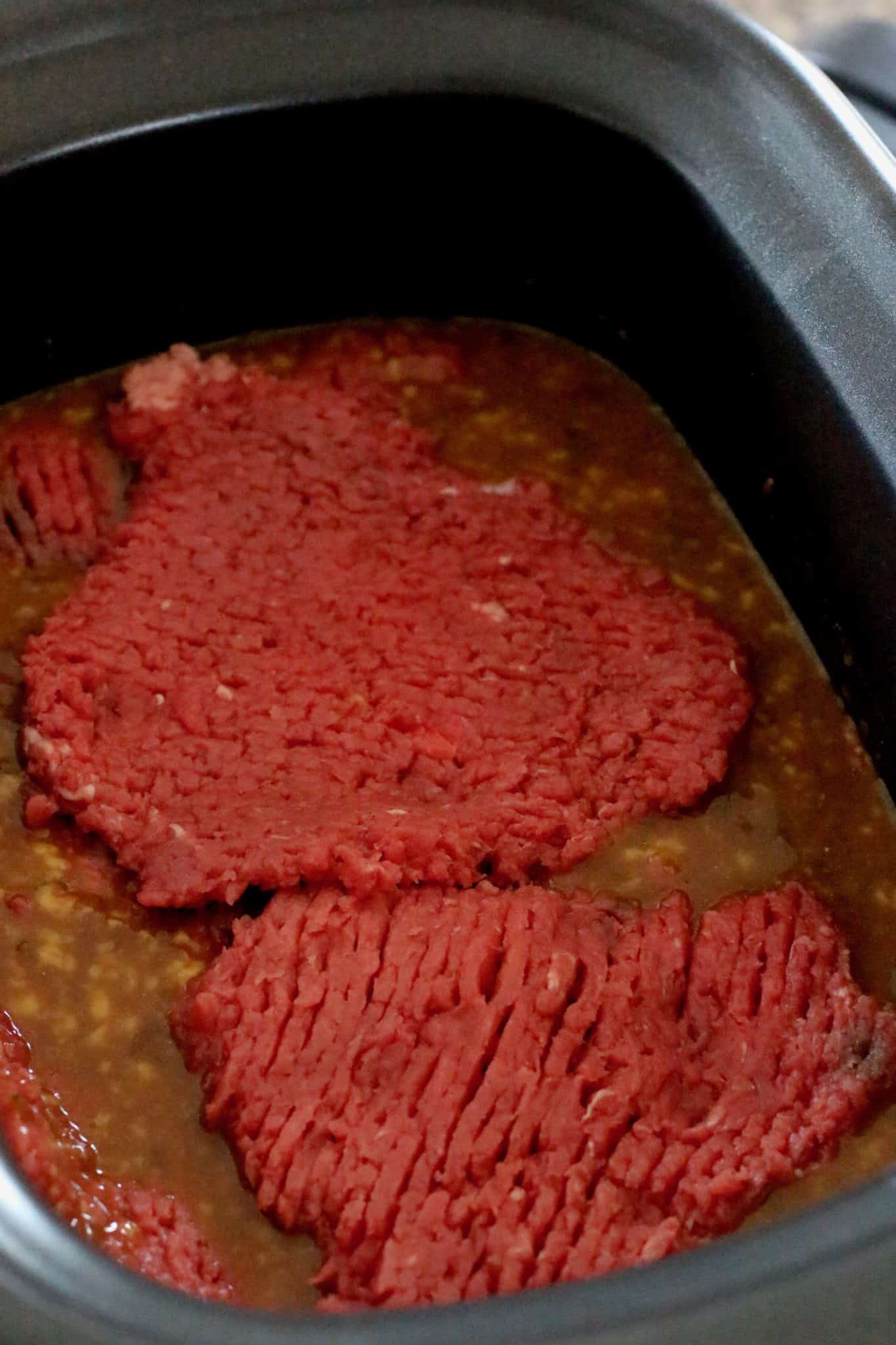 cubed steaks placed in gravy mixture in oval slow cooker.