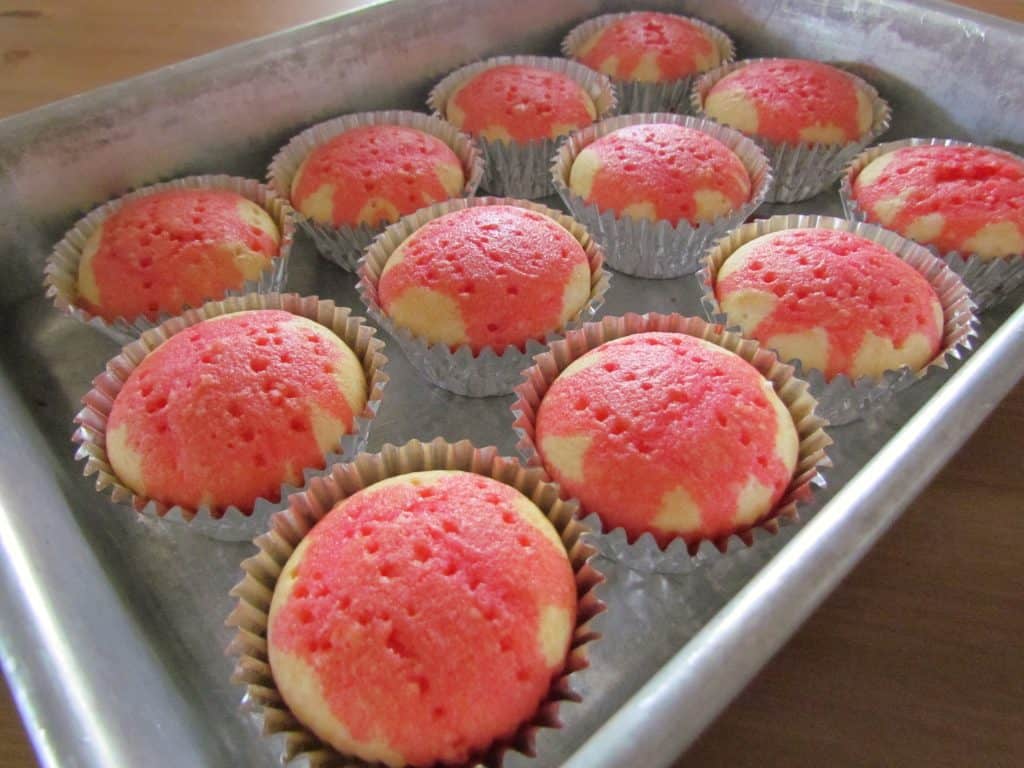 a dozen cupcakes that have been poked with strawberry jell-o in a pan
