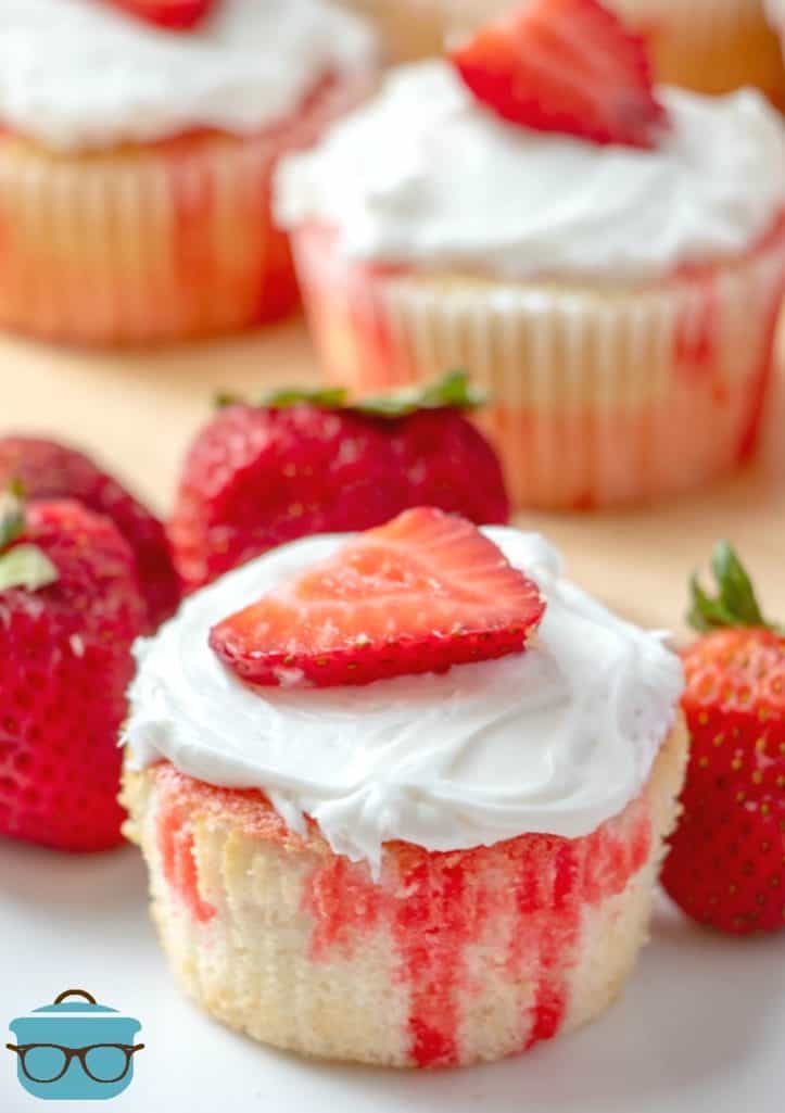 Strawberry Jell-o Poke Cupcakes topped with whipped frosting and a fresh strawberry