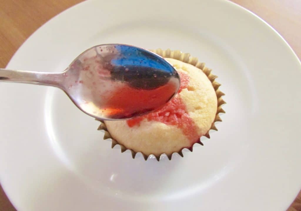 pouring prepared strawberry jello liquid into holes poked in cupcake