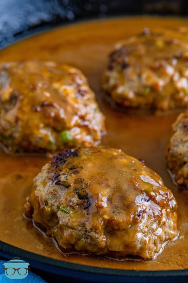four hamburger patties in a cast iron pan and covered in gravy.