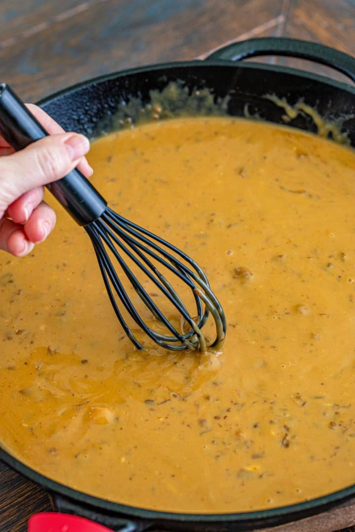 a whisk mixing together gravy mix in cast iron pan.