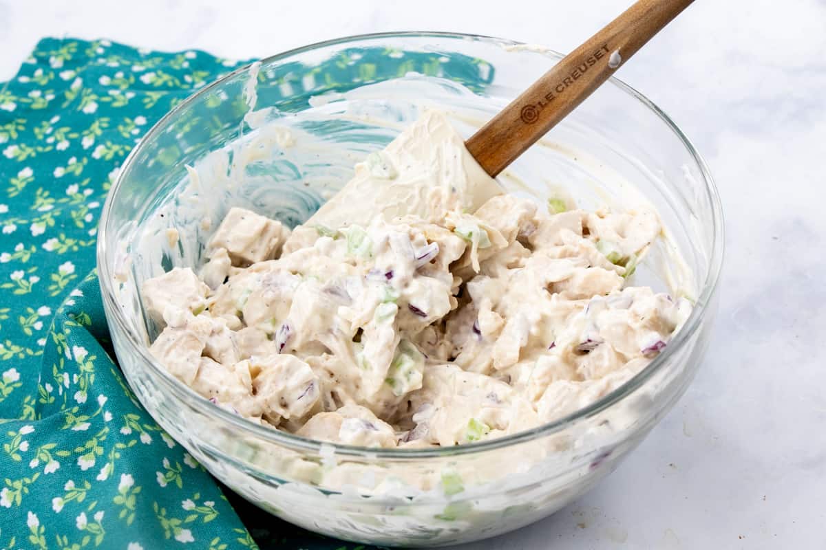 diced chicken added to mayonnaise, sour cream, celery and diced onion in a bowl.