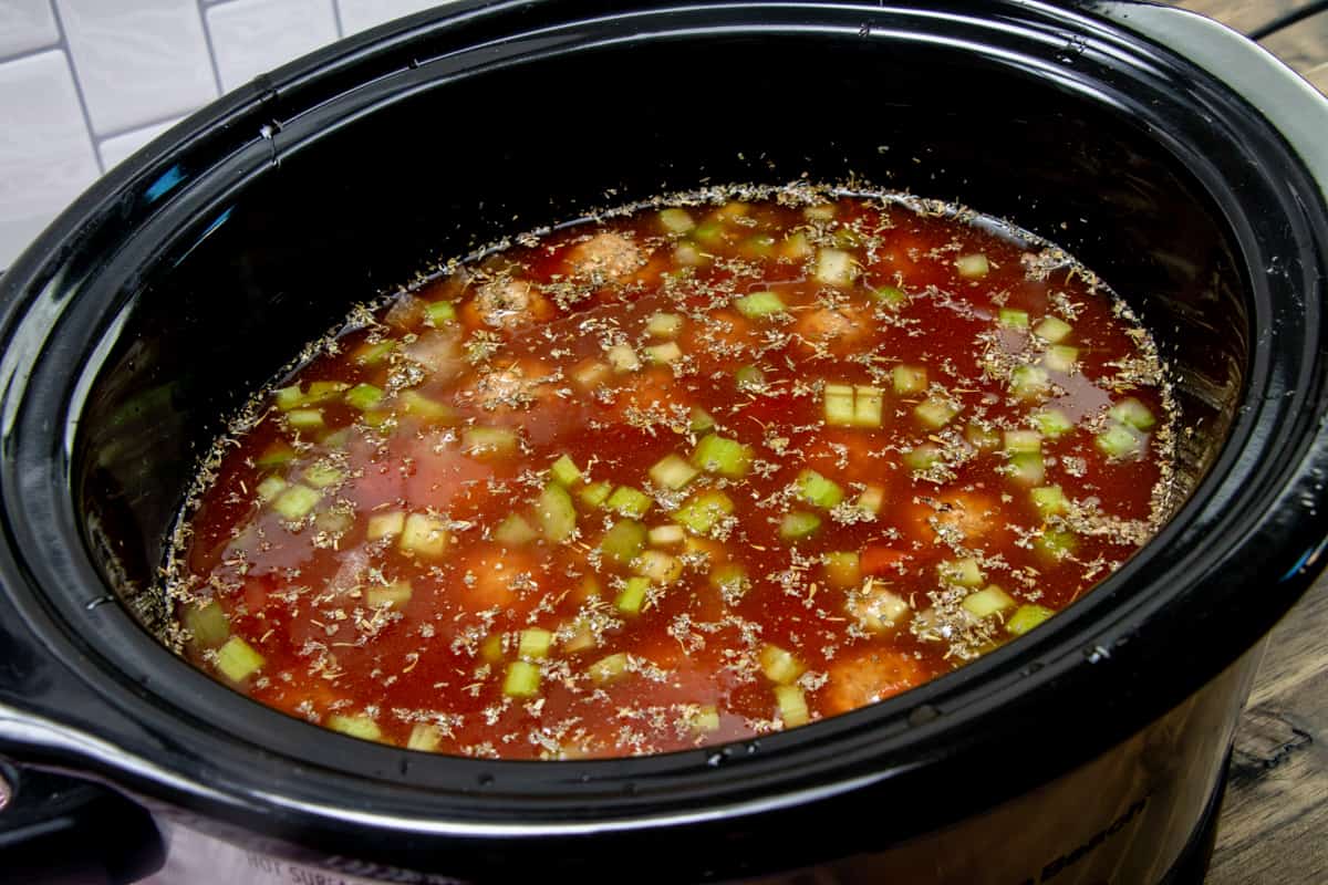 A 5-quart oval slow cooker, filled with beef broth, beans, diced tomatoes, onion, garlic, celery, Italian seasoning and frozen meatballs.