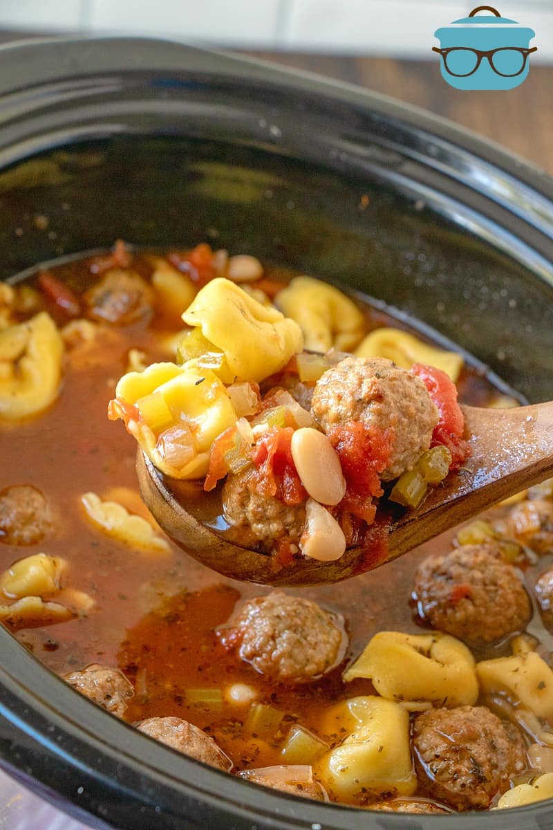 wooden serving spoon with serving of meatball tortellini soup held over slow cooker.