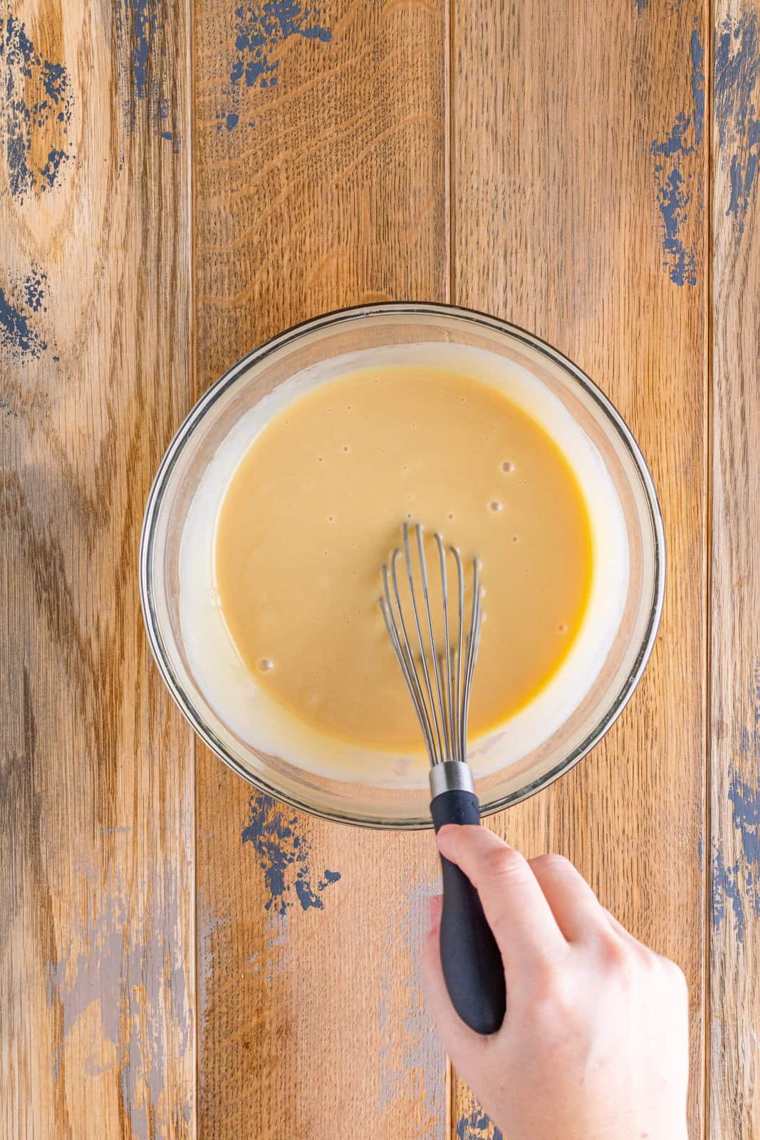 a whisk stirring together sauce ingredients in a clear bowl.