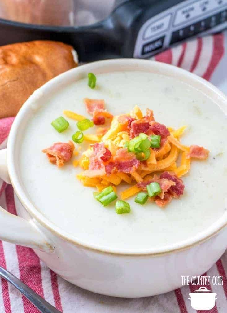 Crock Pot Loaded Potato Soup served in a white bowl with a pice of bread on the side.