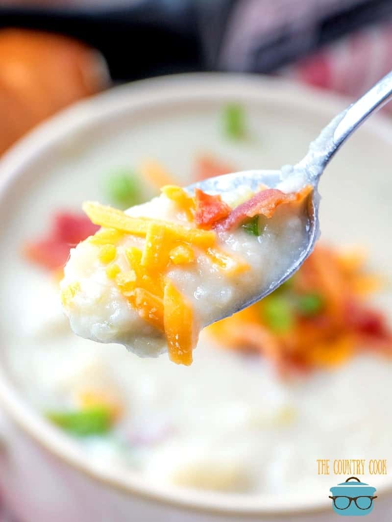 a spoon holding up potato soup over a bowl.