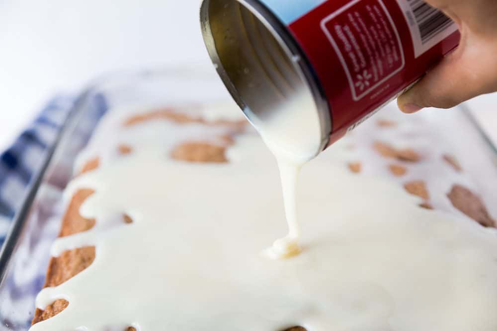 pouring sweetened condensed milk onto baked cake.