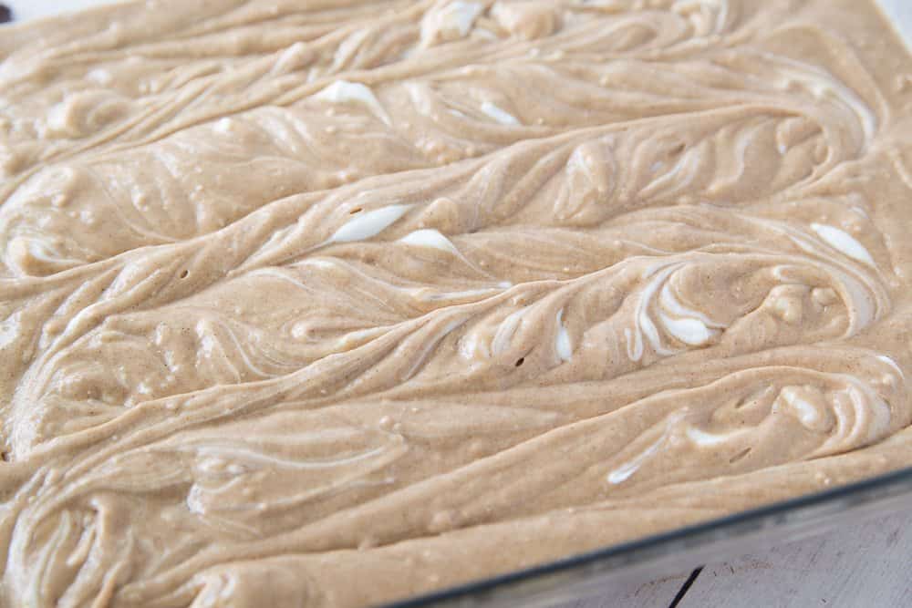 cream cheese batter that has been swirled into spice cake batter in baking dish.