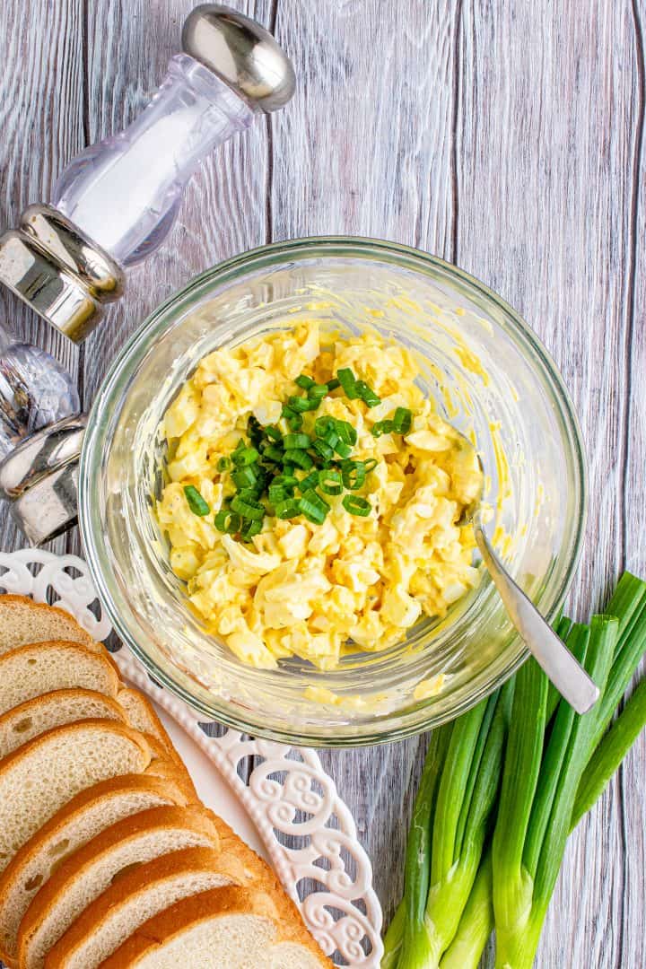 sliced green onion stirred into egg salad in a bowl.