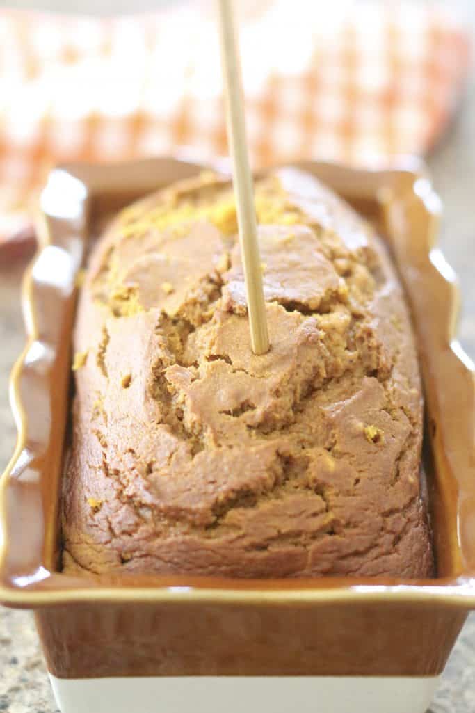 poking holes in baked pumpkin bread with a wooden skewer.