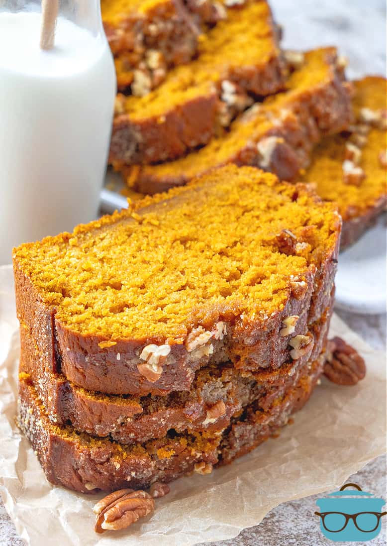Homemade Pumpkin bread, slices shown stacked on parchment paper with a bottle of milk in the background.