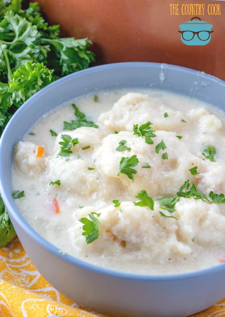 chicken and dumplings shown in a blue bowl and topped with freshly chopped parsley. 