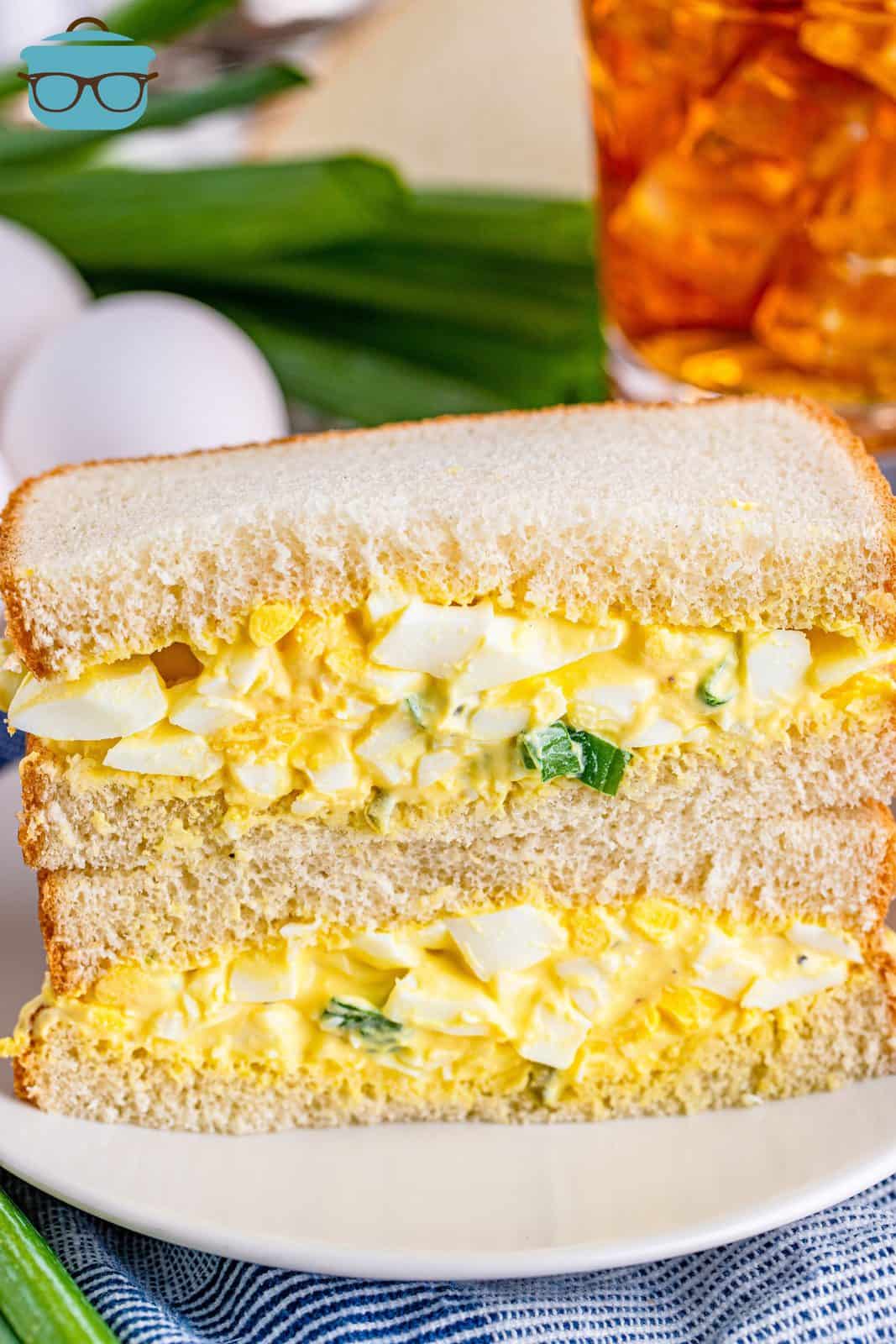 two egg salad sandwiches stacked on top of each other on a white plate.