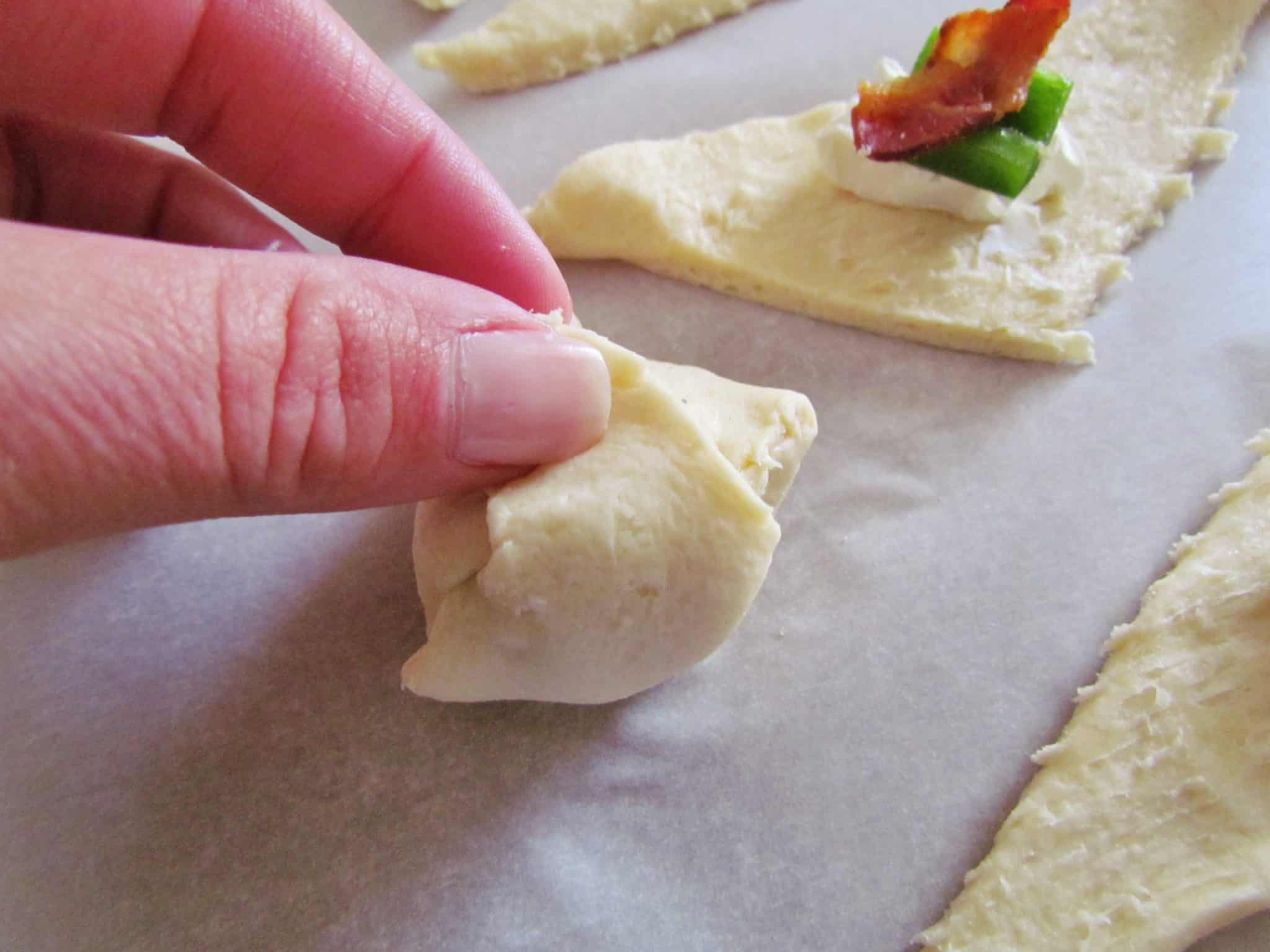 rolling up crescent roll dough to cover cream cheese filling.