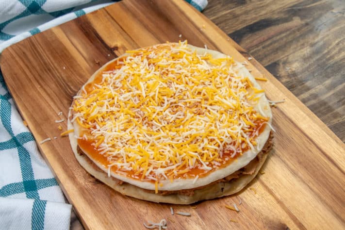 enchilada sauce and shredded cheese placed on top later of fried tortillas