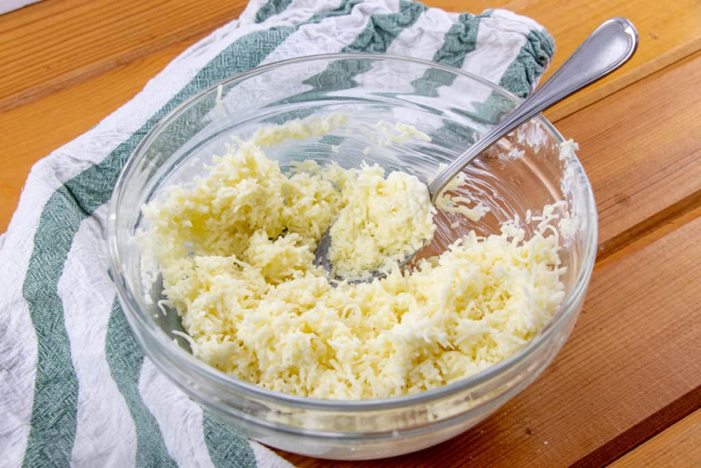 shredded mozzarella cheese and mayonnaise mixed together with a spoon in a glass bowl